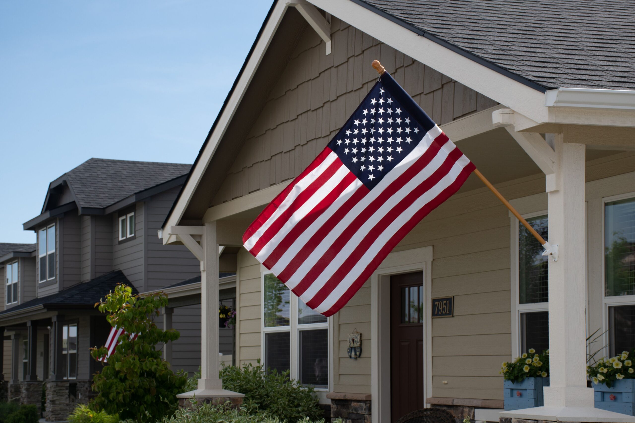 A vibrant American flag displayed outside a stylish suburban house in daylight.